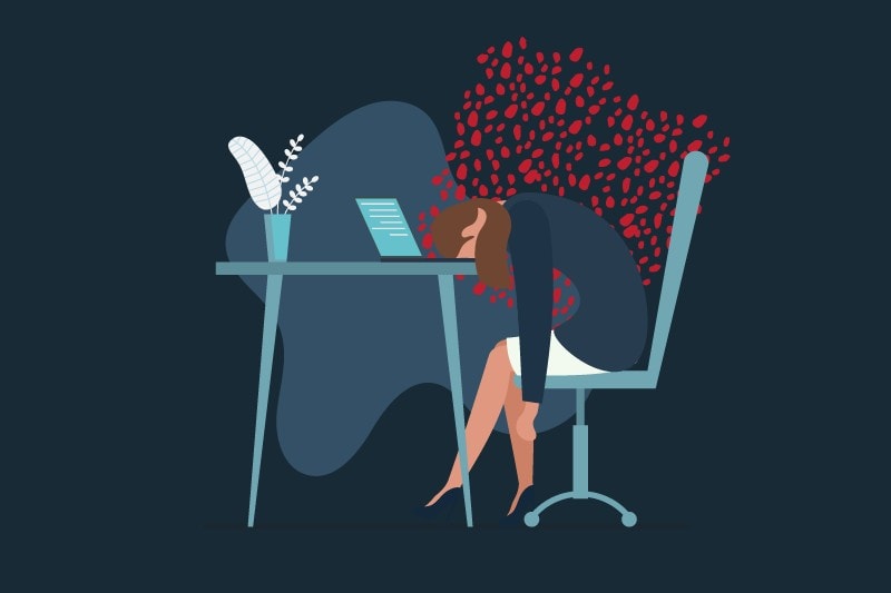 A stressed out woman with her head down at at her work desk feeling overwhelmed.